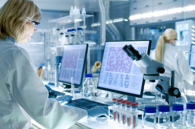 Senior Female Scientist Works with High Tech Equipment in a Modern Laboratory. Her Colleagues are Working Beside Her.