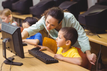 A teacher tutoring a child near a computer