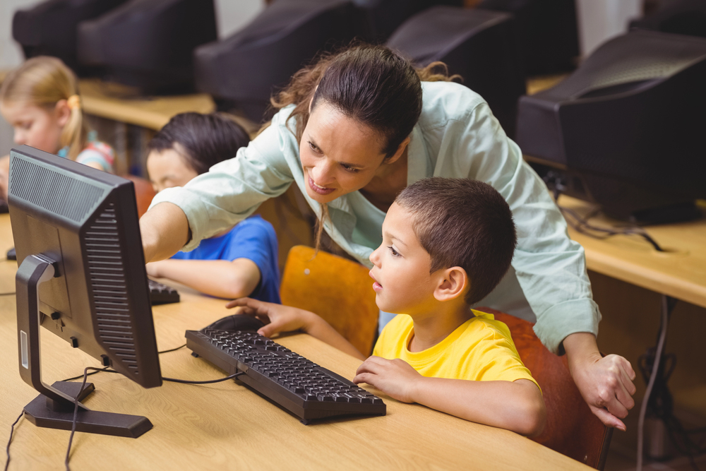 A teacher tutoring a child near a computer
